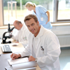 Mature male doctor writing at desk, smiling, portrait