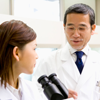 Male scientist talking to female scientist sitting in front of a microscope, front view, side view