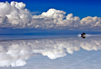 A four wheel drive car driving on the Uyuni Salt Pans in Bolivia with clouds reflected in the thin film of water on the salt