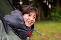 Young girl wrapped in sleeping bag looking out of tent. Camping in forest